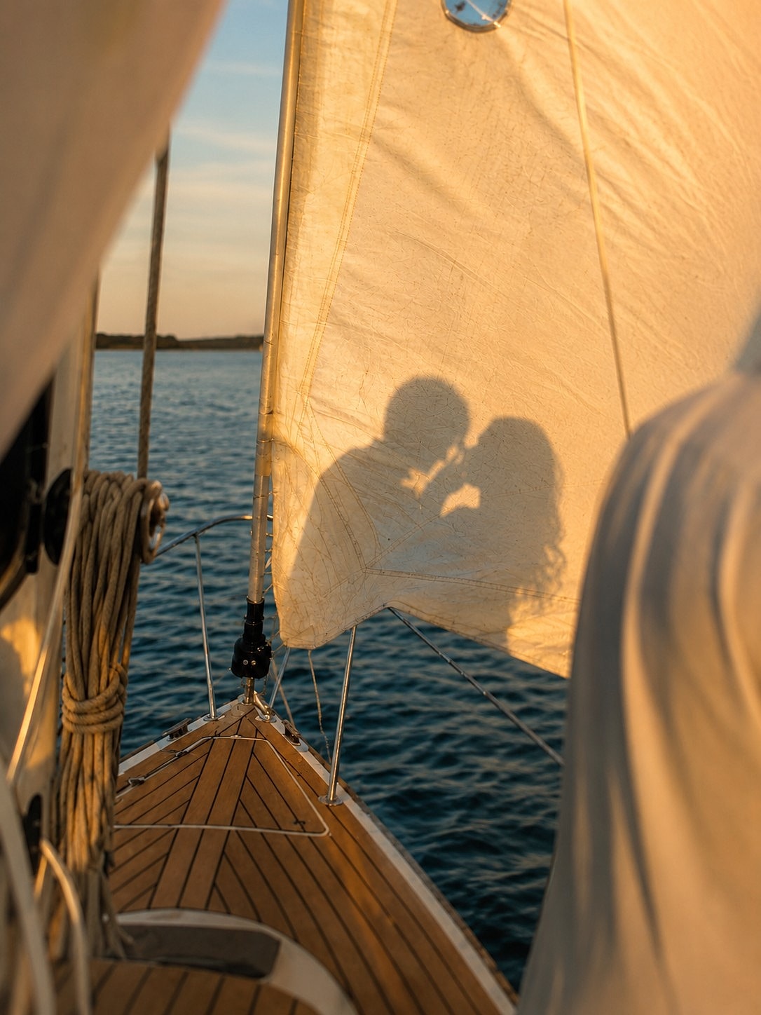 Couple kissing, silhouetted on a sailboat.