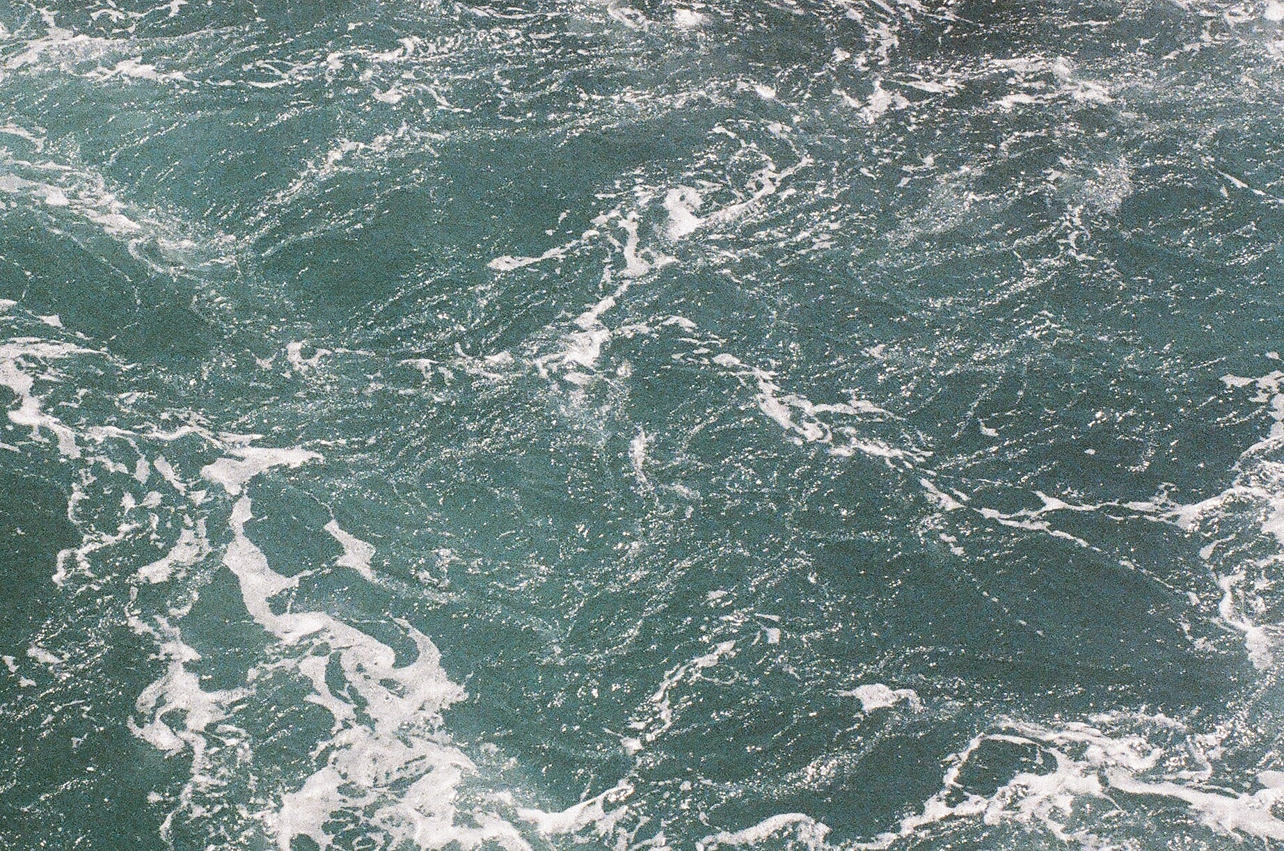 Turquoise ocean waves with white foamy patterns.