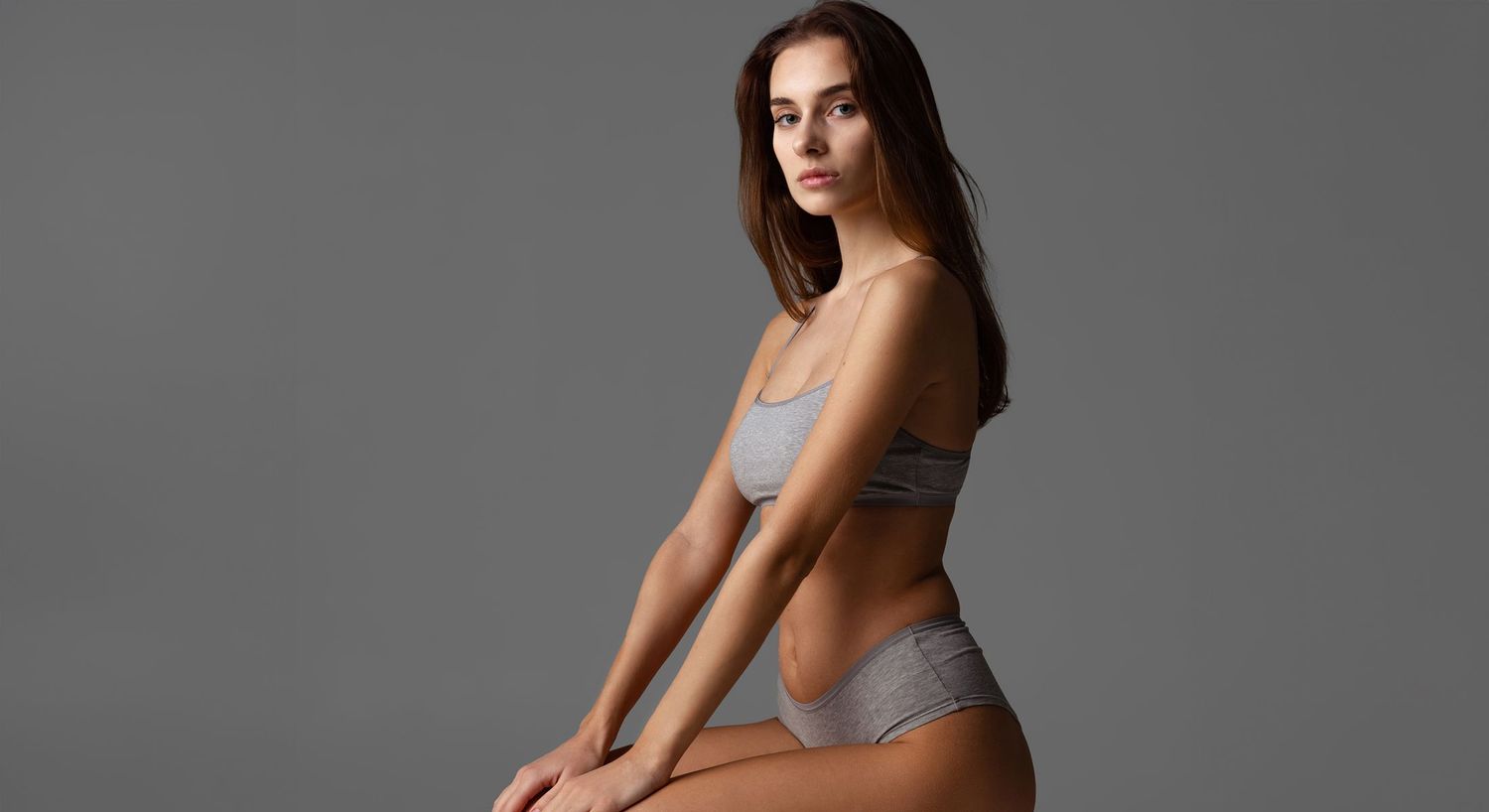 Model in gray lingerie against neutral background.