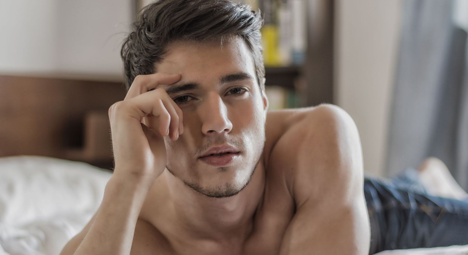 Young man lying on bed, thoughtful expression.